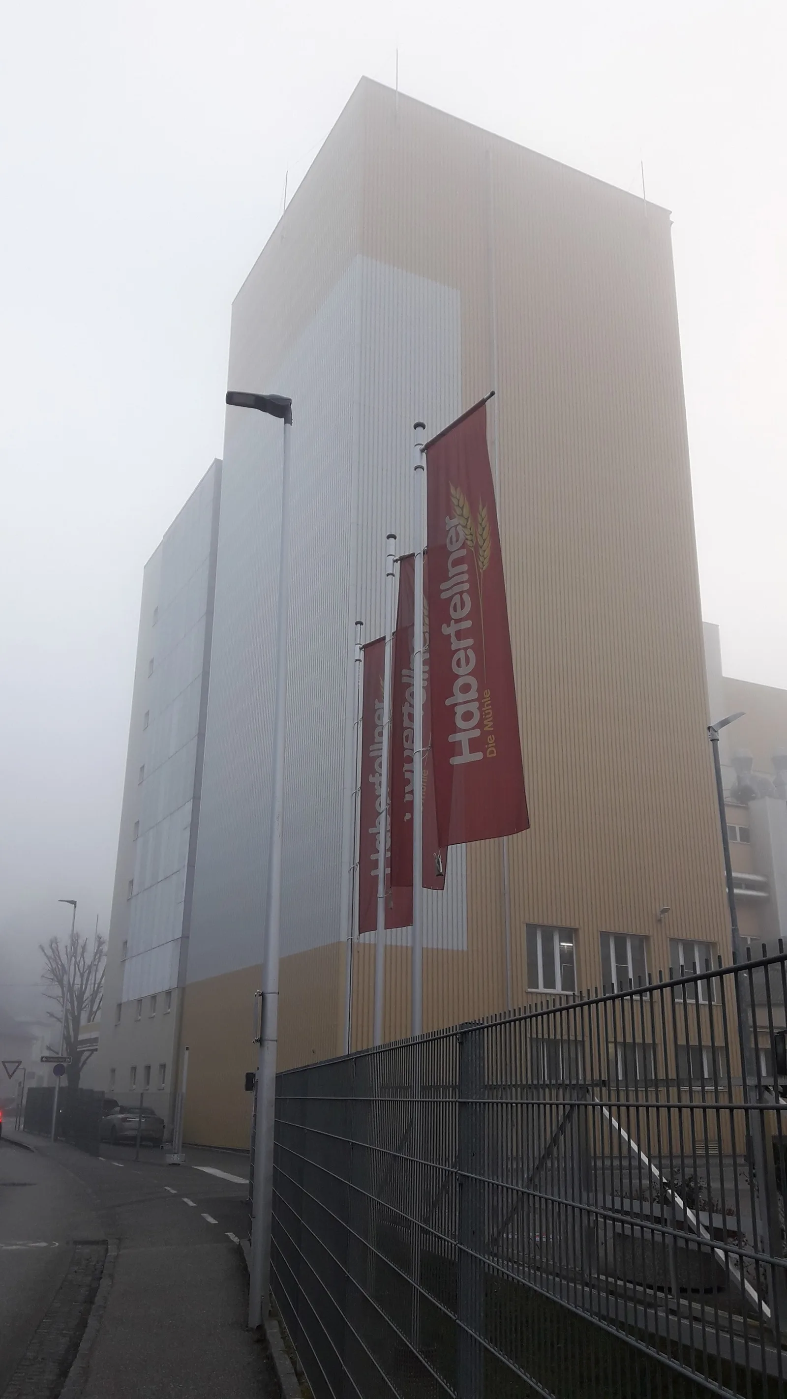 Hoher Siloturm der Mühle mit roten Fahnen im Nebel