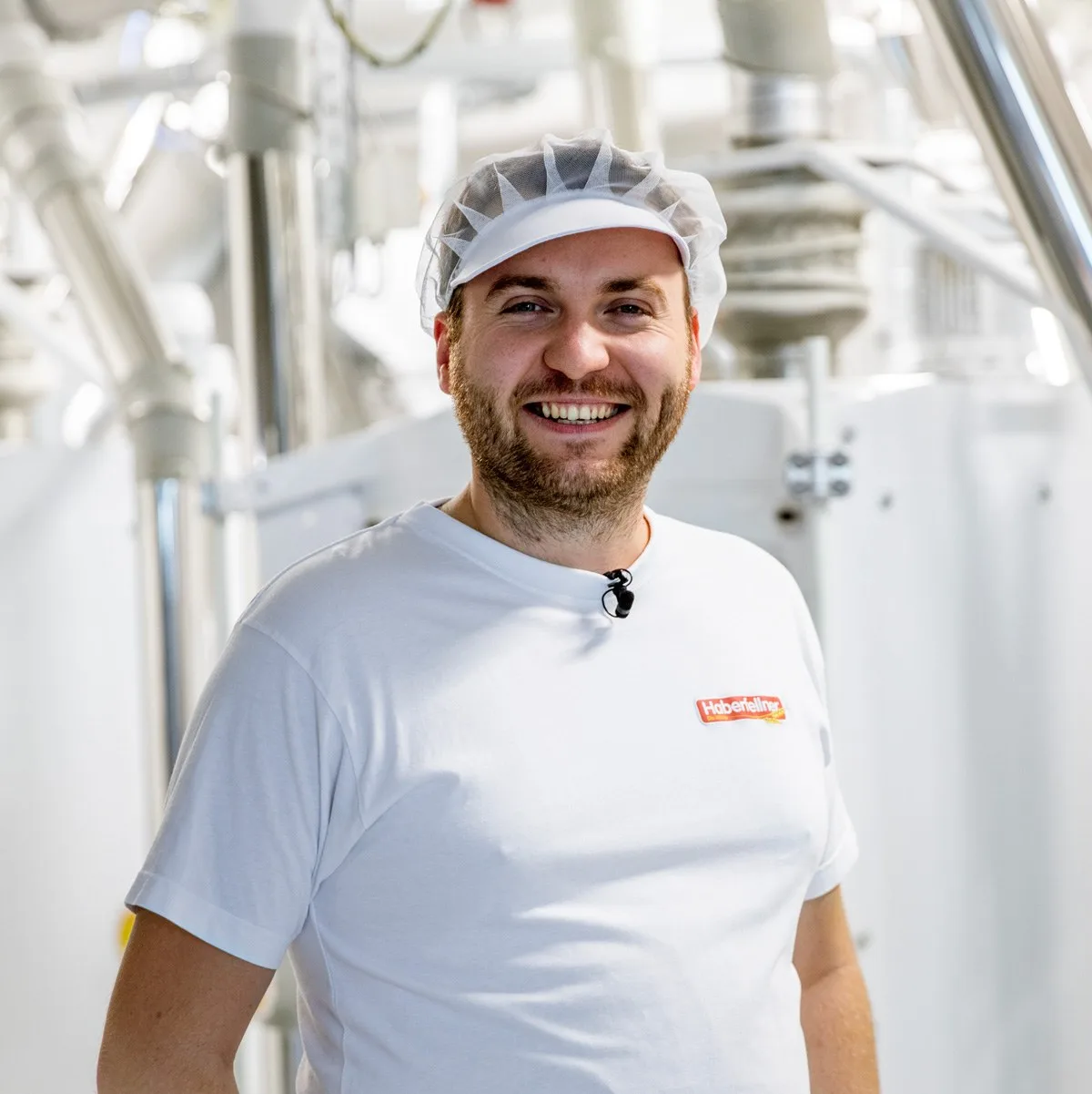 Lachender Mitarbeiter mit Haarnetz und Haberfellner-Shirt in der Mühle